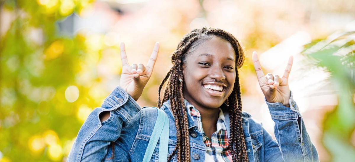 Female student smiling outside holding up the wolf hand sign.